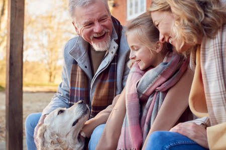 Grandparents With Granddaughter And Pet Dog Outside House Getting Ready To Go For Winter Walkの写真素材