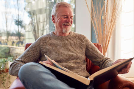 Smiling Senior Man At Home Enjoying Looking Through Photo Album Together
