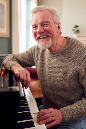 Portrait Of Senior Man At Home Enjoying Learning To Play Piano
