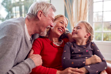 Loving Grandparents Hugging Granddaughter Sitting On Sofa At Home Together