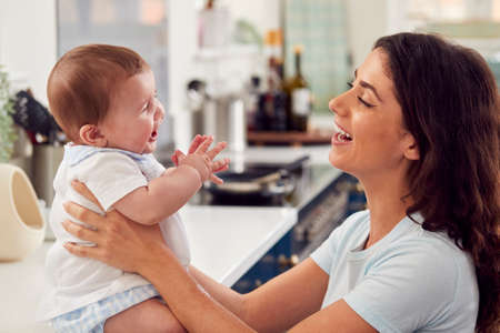 Loving Mother Caring For Baby Son At Home In Kitchen Togetherの写真素材