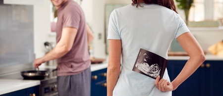 Pregnant Transgender Couple At Home In Kitchen With Woman Surprising Man With Ultrasound Scan Of Babyの写真素材