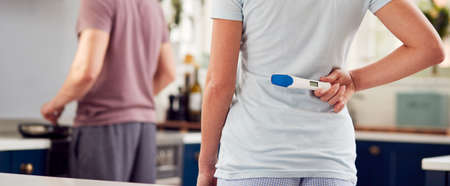 Transgender Couple At Home In Kitchen With Woman Surprising Man With Positive Pregnancy Test