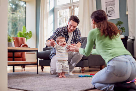 Transgender Family Encouraging Baby To Take First Steps In Lounge At Homeの写真素材
