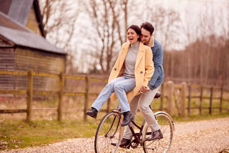 Loving Transgender Couple With Woman Riding On Handlebars Of Bike In Autumn Or Winter Countrysideの写真素材