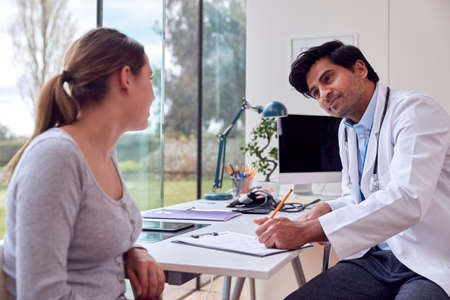 Male Doctor Or GP Wearing White Coat Examining Teenage Girl Listening To Chest With Stethoscopeの写真素材