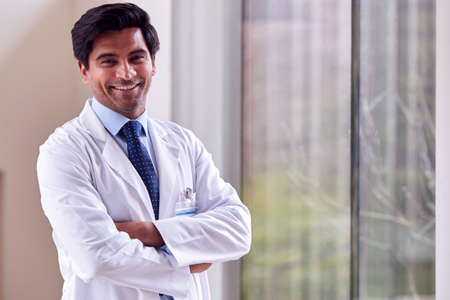 Portrait Of Male Doctor Wearing White Coat Standing In Hospital Corridorの写真素材