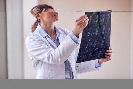 Female Doctor Wearing White Coat Standing In Hospital Corridor Looking At CT Or MRI Scan