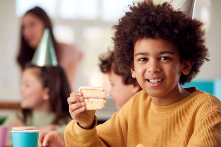 Portrait Of Boy Eating Birthday Cake At Party With Parents And Friends At Home