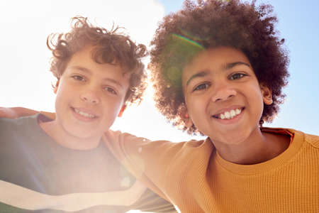 Low Angle Portrait Of Two Boys Having Fun Playing Outdoors Looking Down Into Camera With Lens Flareの写真素材