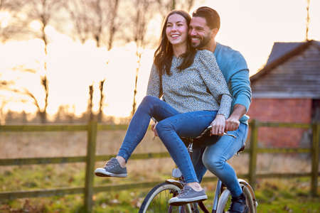 Couple Riding Bike Through Countryside With Woman Sitting On Handlebarsの写真素材