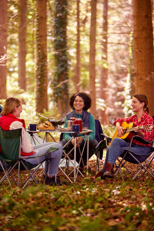 Group Of Female Friends On Camping Holiday In Forest Eating Meal And Singing Along To Guitarの写真素材
