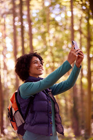 Woman Taking Photo On Mobile Phone On Holiday Hiking Through Woods