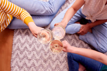 Close Up Of Female Friends Relaxing At Home Sitting In Lounge Celebrating With Glass Of Wineの写真素材