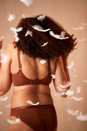 Rear View Of Feathers Falling On Confident Natural Woman In Underwear Promoting Body Positivityの写真素材