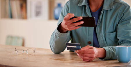 Close Up Of Man With Credit Card At Home Using Mobile Phone To Check Finances For Starting Business