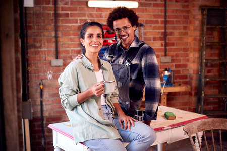 Couple Running Business In Workshop At Home Restoring And Upcycling Furniture On Coffee Break