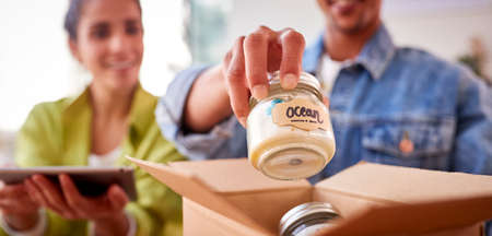 Close Up Of Couple Running Online Business From Home Packing Boutique Candles Ready For Shipping