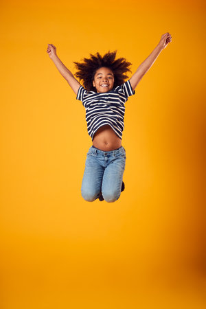 Studio Shot Of Energetic Boy Jumping In The Air With Outstretched Arms Against Yellow Backgroundの写真素材