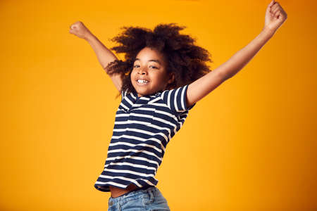 Studio Shot Of Energetic Boy Jumping In The Air With Outstretched Arms Against Yellow Background