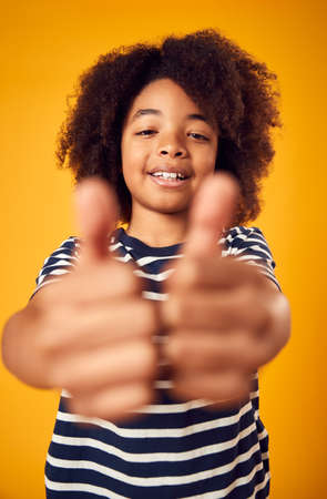 Studio Portrait Of Smiling Young Boy Making Thumbs Up Gesture Shot Against Yellow Backgroundの写真素材