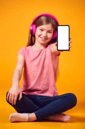 Studio Portrait Of Girl With Headphones Streaming Music From Mobile Phone Against Yellow Backgroundの写真素材