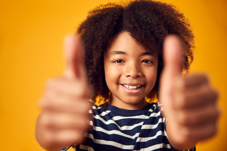 Studio Portrait Of Smiling Young Boy Making Thumbs Up Gesture Shot Against Yellow Backgroundの写真素材