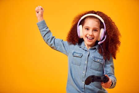 Studio Portrait Of Girl With Headphones Playing Computer Game Against Yellow Backgroundの写真素材