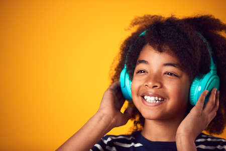 Studio Shot Of Smiling Young Boy Listening To Music On Headphones Against Yellow Backgroundの写真素材