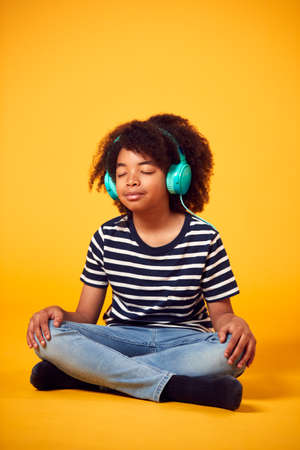Studio Shot Of Boy With Eyes Closed Listening To Music On Headphones Against Yellow Backgroundの写真素材