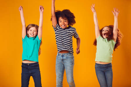 Studio Shot Of Energetic Children Jumping In The Air With Outstretched Arms On Yellow Backgroundの写真素材