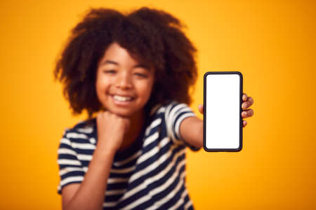 Studio Portrait Of Boy Showing Mobile Phone With Social Media Screen Against Yellow Backgroundの写真素材