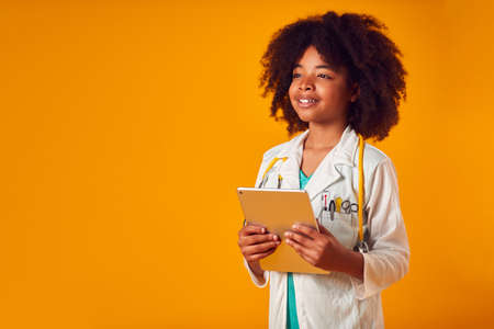 Studio Portrait Of Boy Dressed As Doctor Or Surgeon With Digital Tablet Against Yellow Backgroundの写真素材