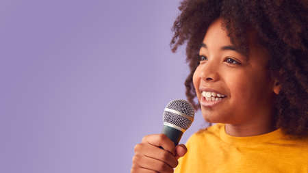 Studio Shot Of Boy Singing Karaoke Into Microphone Against Purple Backgroundの写真素材