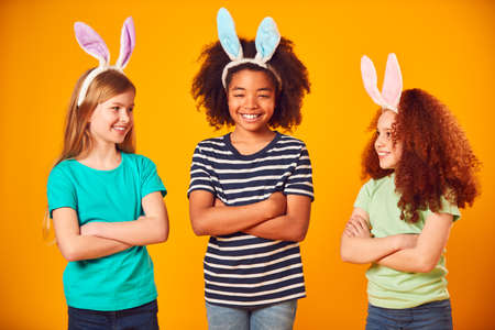 Studio Portrait Shot Of Three Children Friends Wearing Easter Rabbit Ears Against Yellow Background