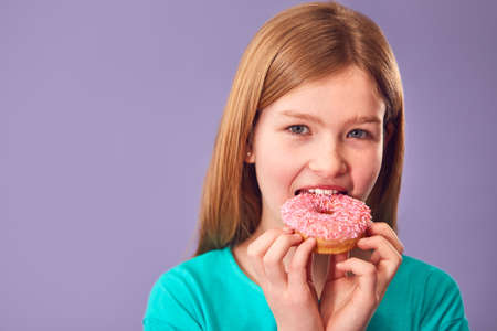 Studio Portrait Of Girl Eating Donut Against Purple Backgroundの写真素材