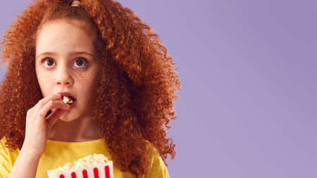 Scared Girl Watching Horror Movie And Eating Popcorn At Cinema Against Purple Background
