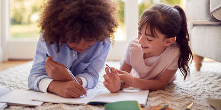 Boy And Girl Lying On Rug In Lounge At Home Doing School Homework Togetherの写真素材