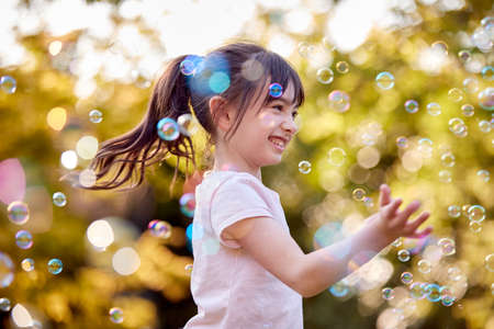 Smiling Girl Outdoors Having Fun Playing With Bubbles In Gardenの写真素材