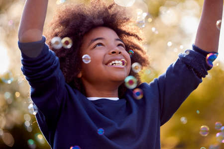 Smiling Boy Outdoors Having Fun Playing With Bubbles In Garden
