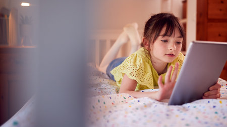 Girl In Bedroom Lying On Bed Enjoying Using Digital Tabletの写真素材