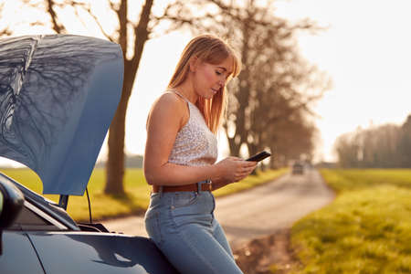 Woman With Broken Down Car On Country Road Calling For Help On Mobile Phone