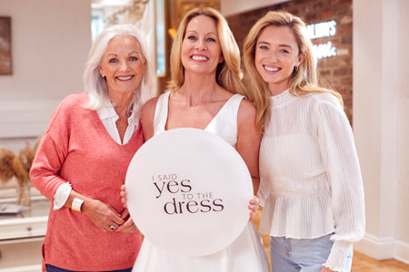 Grandmother With Adult Daughter And Granddaughter In Bridal Store Holding "Yes To The Dress" Signの写真素材