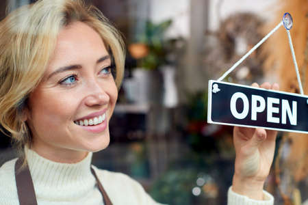 Smiling Female Owner Of Small Business Turning Round Open Sign In Shop Windowの写真素材