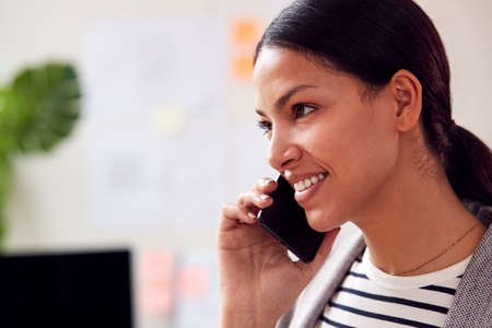 Close Up Of Female Architect Working Standing In Office Talking On Mobile Phone
