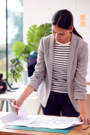 Female Architect Standing Working In Office Studying Plans For New Buildingの写真素材