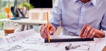 Close Up Of Mature Male Architect Working In Office At Desk Studying Plans For New Building