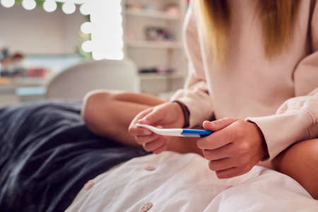 Close Up Of Teenage Girl Sitting On Bed At Home Looking At Positive Pregnancy Testの写真素材
