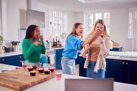 Group Of Teenage Girls Eating And Having Fun Playing With Cupcakes In Kitchen At Homeの写真素材