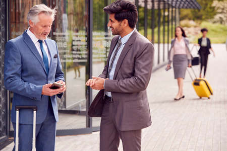 Two Delegates With Luggage Meeting Outside Business Conference Hotel